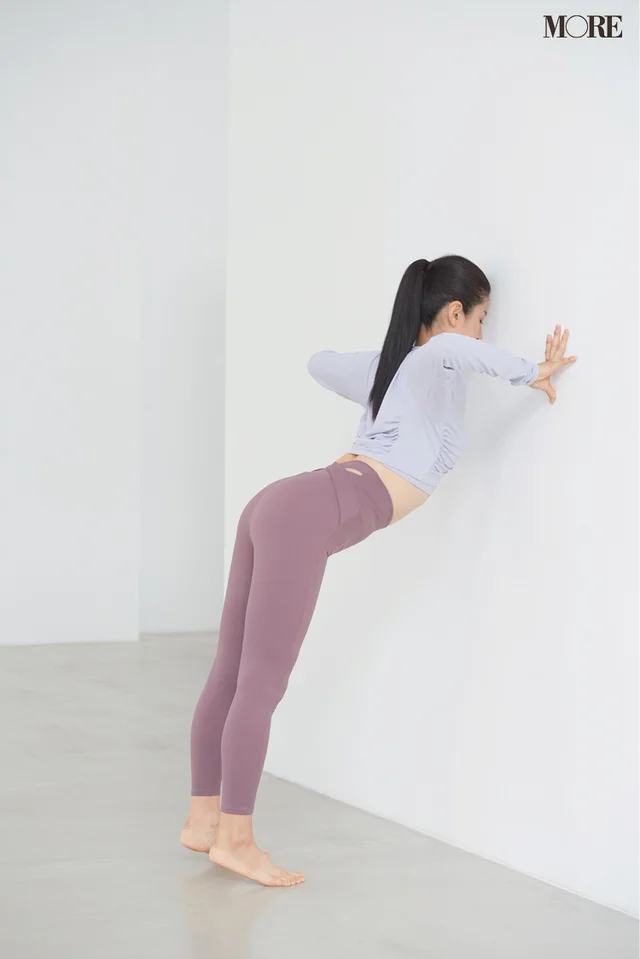 両肘を真横に開いて曲げて胸を壁に近づけながらお尻を締める女性