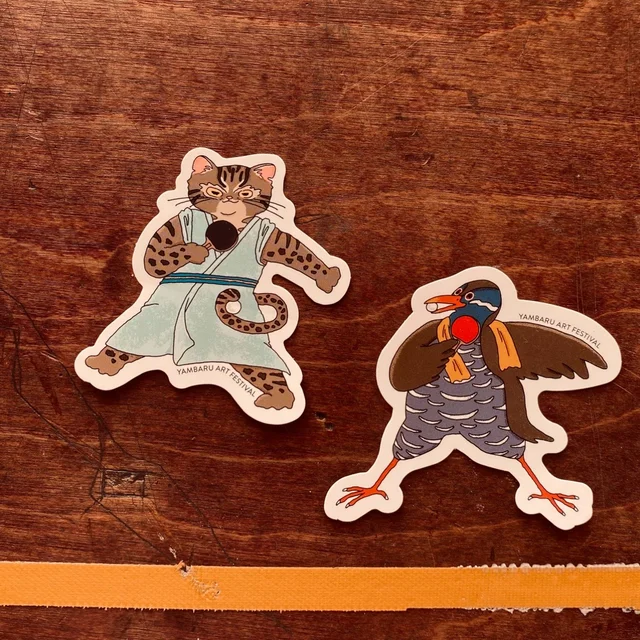 やんばるアートフェスティバル公式グッズ：イリオモテヤマネコとヤンバルクイナの卓球ステッカー