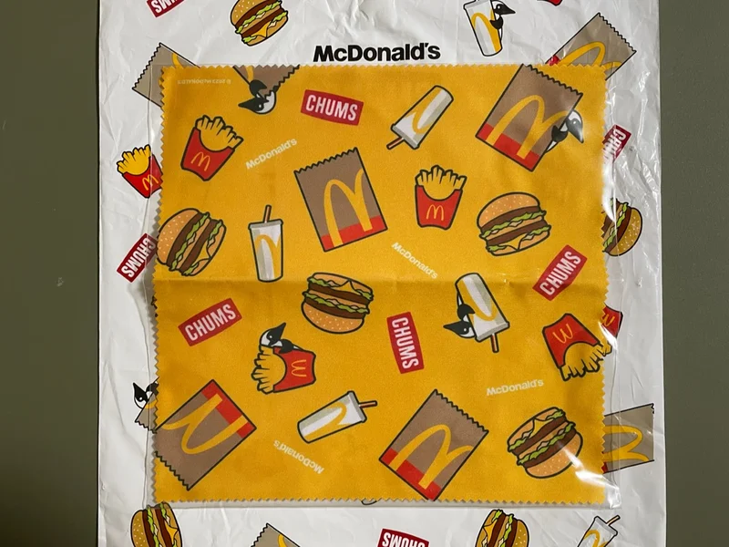 クリーナークロスの写真。マクドナルドのテイクアウトの袋、ポテトの入れ物、ドリンクカップ、ハンバーガーのイラストとCHUMSのロゴがまばらに描かれている。