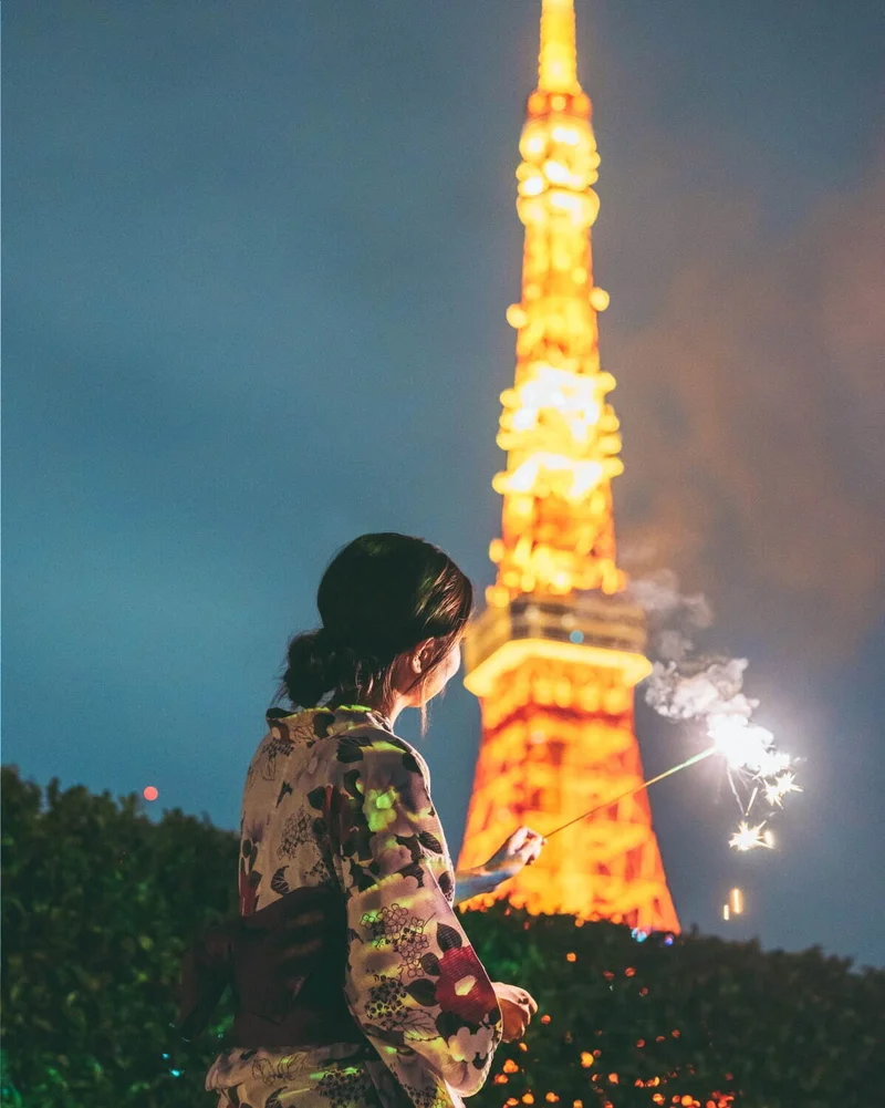 ライトアップされた東京タワーのふもとで、手持ち花火をする浴衣の女性の後ろ姿