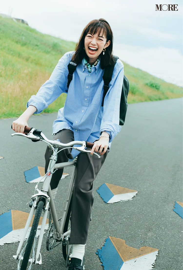 ブルーのシャツ×グレーのパンツコーデで自転車に乗る佐藤栞里