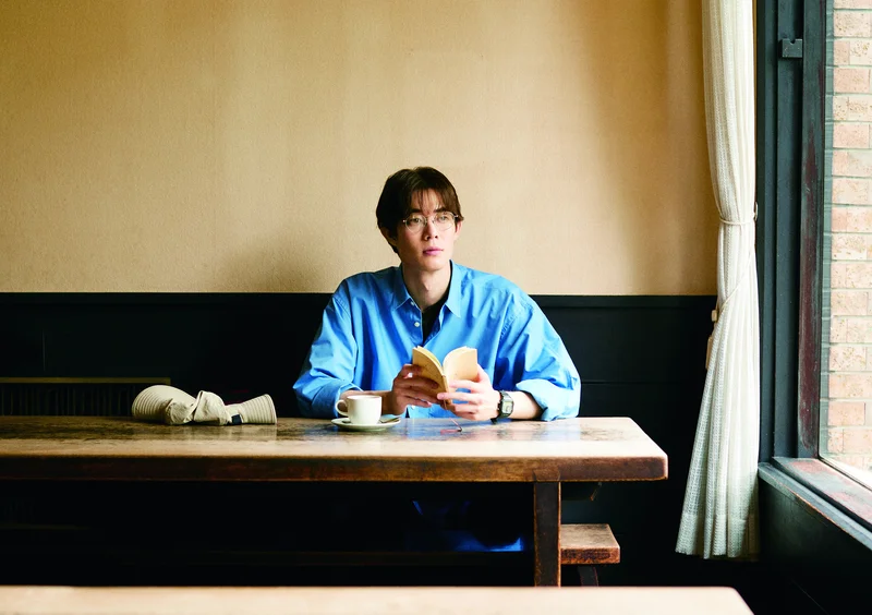 氷魚「特にお気に入りの写真は、京都の喫茶店で本を読んでいるカットです。スタイリングも好きで、青いシャツにメガネをかけて、喫茶店でくつろいでいる。僕の理想の休日だからよけいに思い入れがあります」 ©宮沢氷魚 ファースト写真集 『Next Journey』／集英社　撮影／尾身沙紀（io）