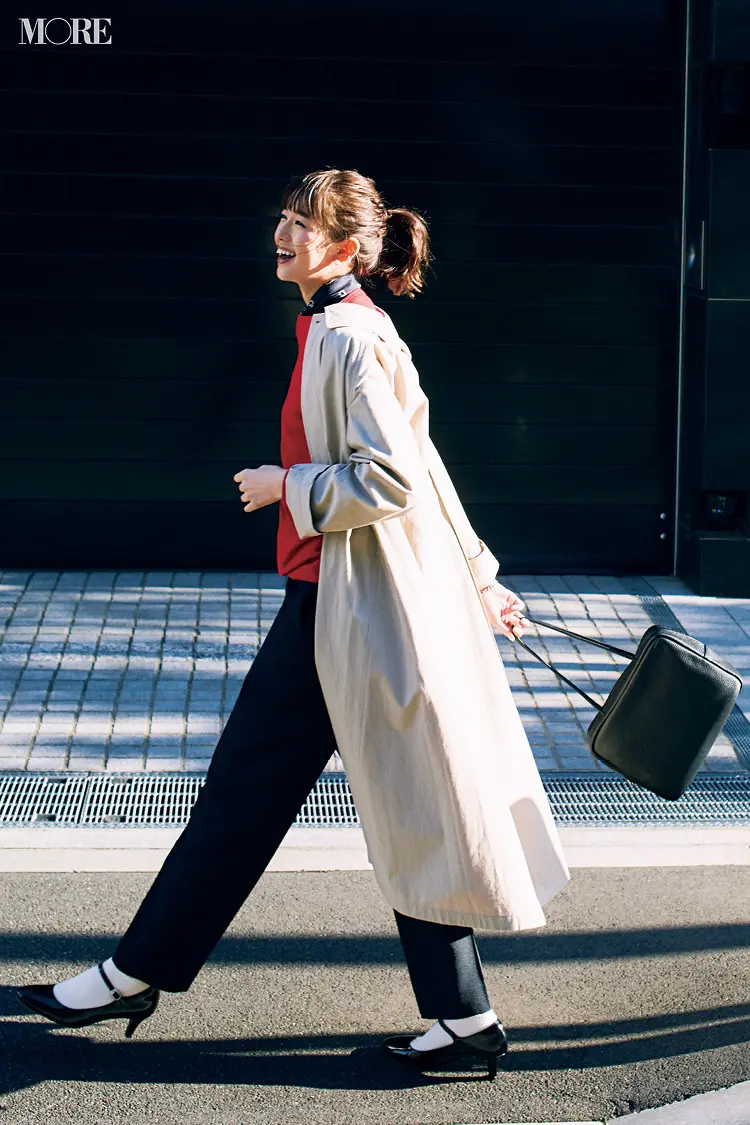 赤トップスと黒パンツにベージュのステンカラーコートをはおった佐藤栞里