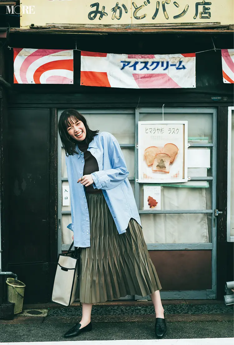 タートルネックニットにシャツをはおってプリーツスカートをはいた佐藤栞里