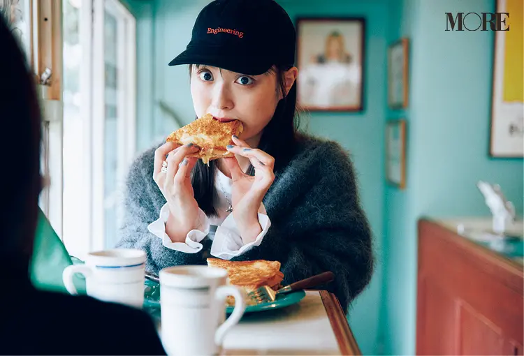 オーバーサイズニットを着てキャップをかぶった内田理央がサンドイッチを食べている